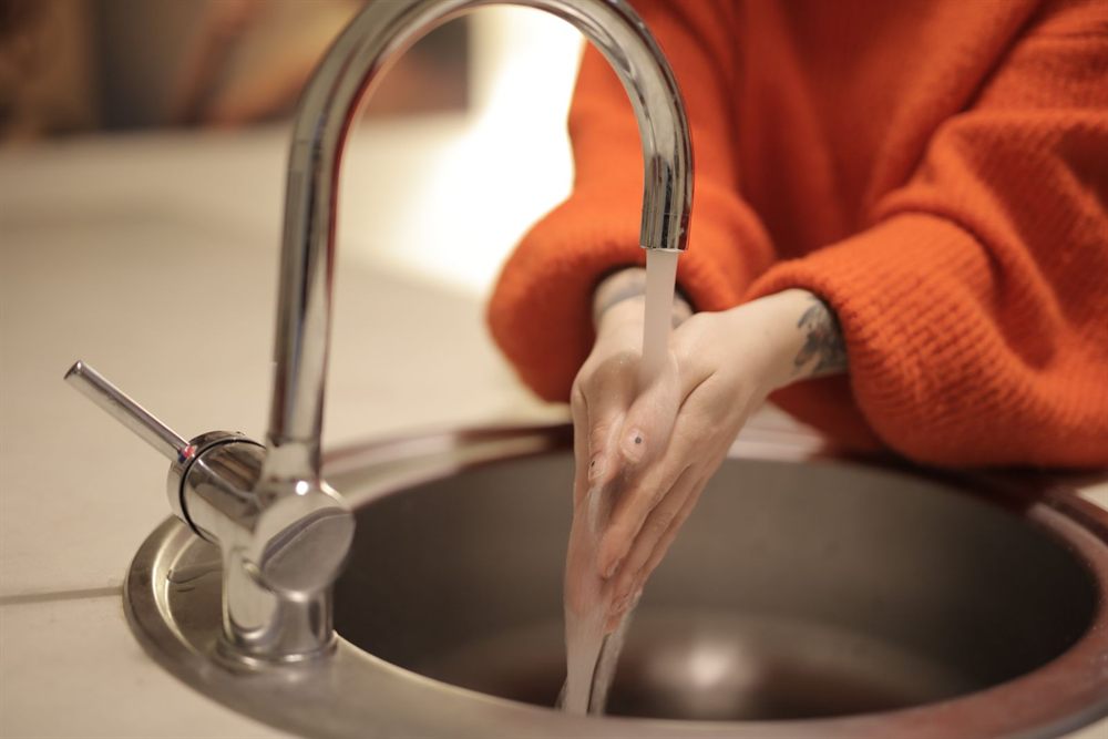 Hands washed under a chrome faucet at a sink