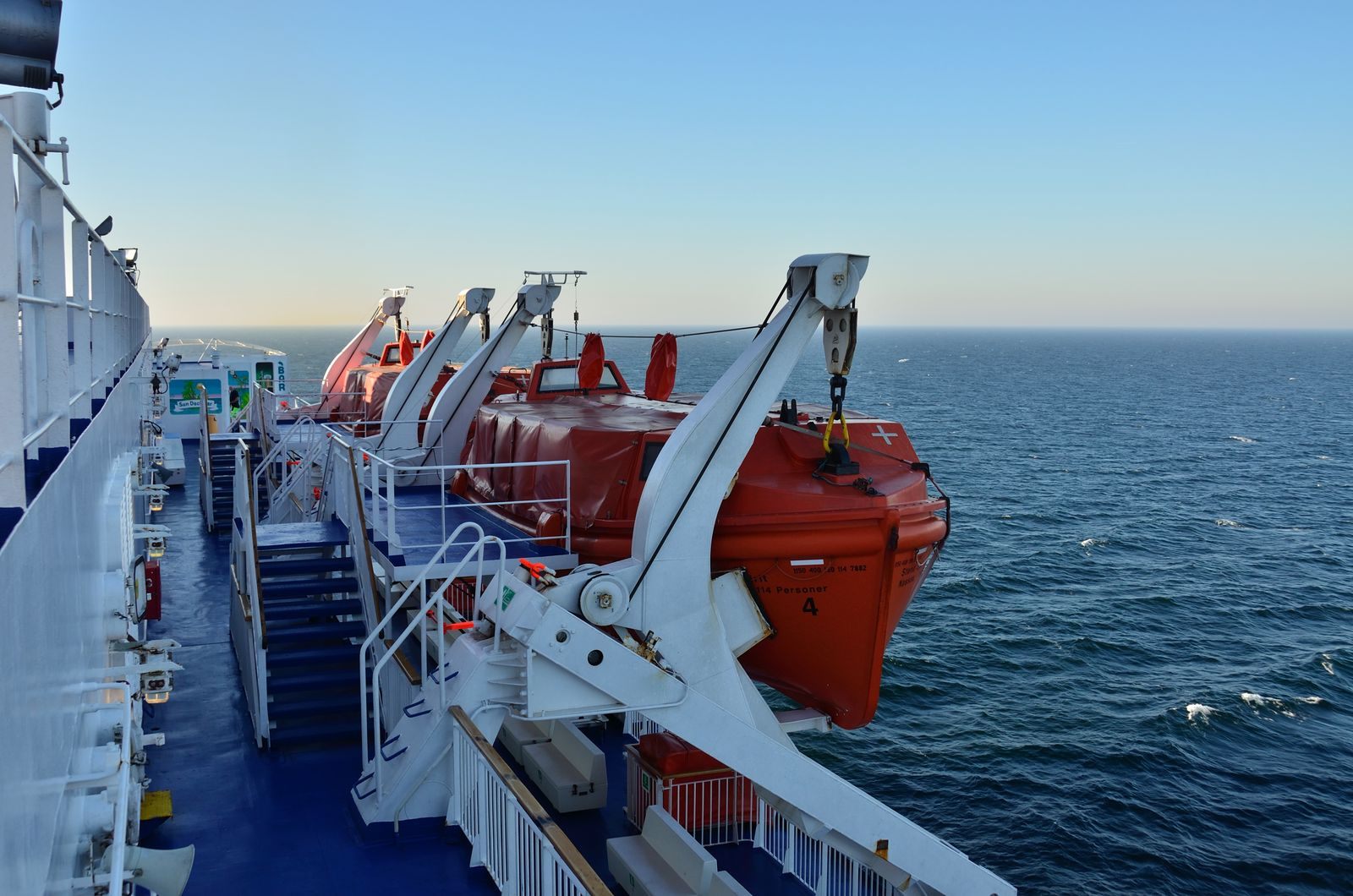 Orange lifeboats along a cruise ship deck above the open sea, part of the answer to how safe are cruises