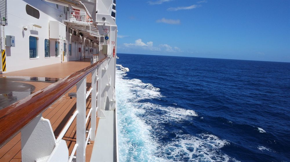 View along a ship side deck and railing over the ocean wake